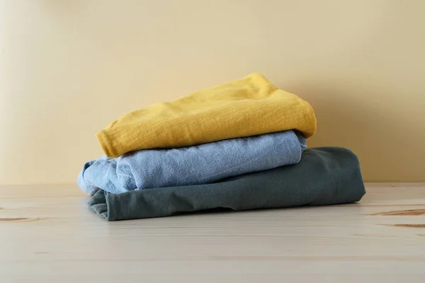 Folded clothes on wooden table and yellow background — Stock Photo, Image