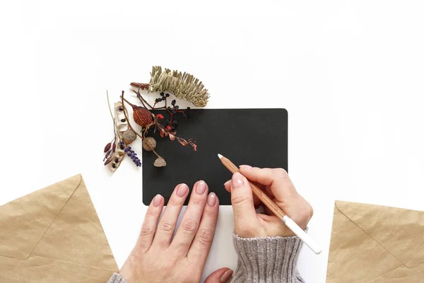 Woman s hands holding white pencil. Black sheet of paper decorated with flowers — Stock Photo, Image