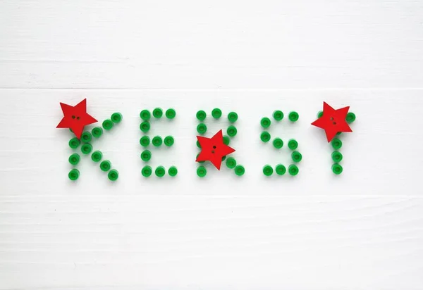 Christmas card in Dutch language. Decorative string beads, green letters and red stars. White wooden background, top-view perspective and text space.