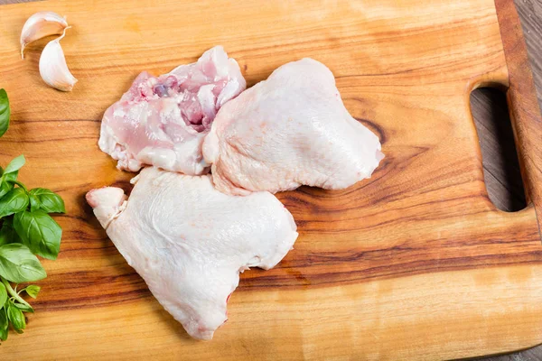 Raw chicken thighs with skin and bone on chopping board with herbs