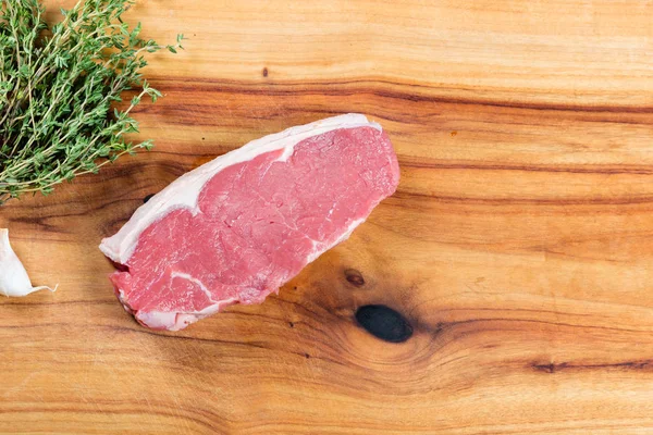 Raw beef sirloin steak on chopping board with herbs