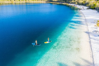 Couple stand up paddle boarding  on Lake Mckenzie, Fraser Island, Queensland, Australia clipart