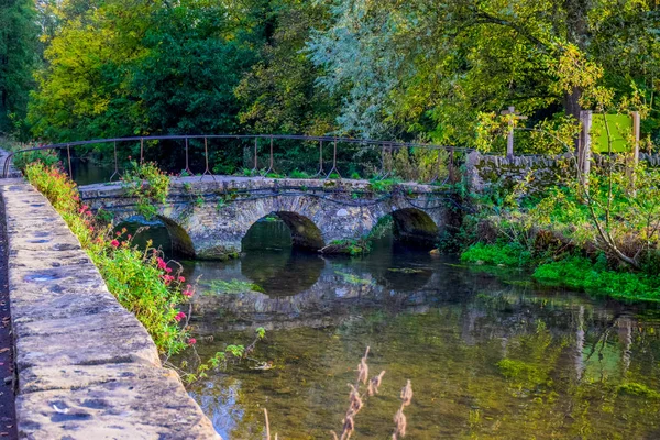 A small vintage stone bridge over river Coln that leads to Arlington Row of Bibury village in Cotswold district, Gloucestershire, England, UK