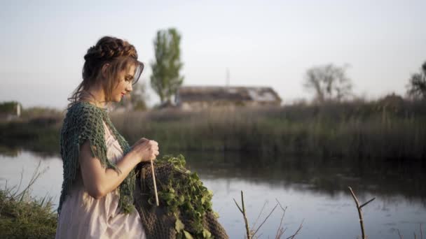 Knitting kobiety strony Dokonywanie Tkaniny wełniane. dziewczyna siedzi na brzegu jeziora — Wideo stockowe
