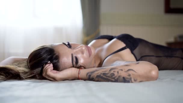 Пристрасна красива модель лежить на ліжку в готелі і позує на фотографії — стокове відео