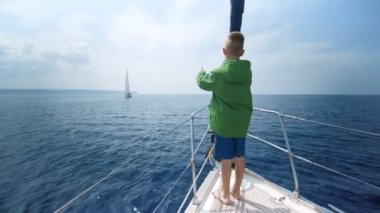 Küçük çocuk yat yay üzerinde duruyor ve yol gösterir