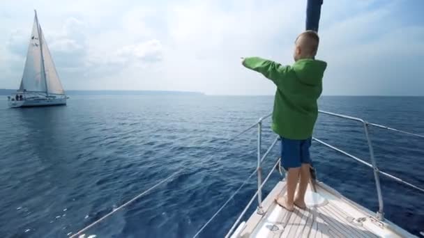 Pequeño niño se para en la proa del yate y muestra el camino — Vídeo de stock