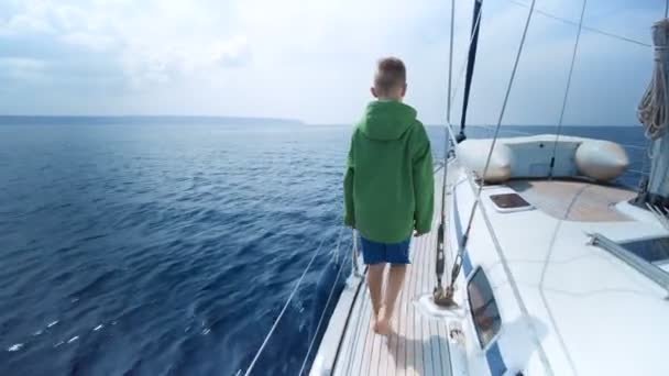 Маленький мальчик стоит на носу яхты и показывает путь — стоковое видео