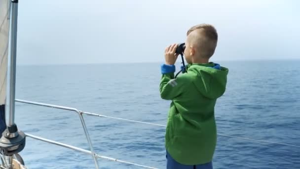 Kleiner Junge steht auf einer Jacht und schaut in ein Fernglas — Stockvideo
