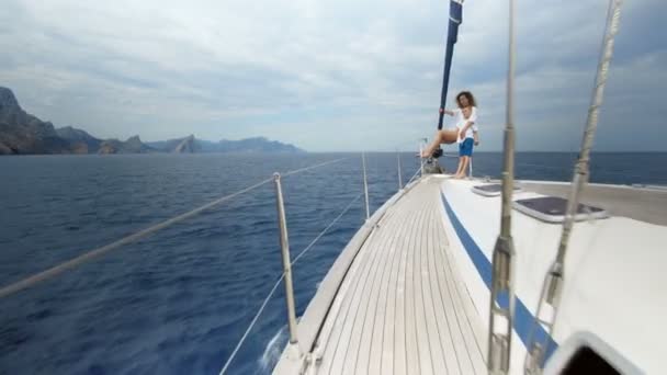 Una hermosa chica mira a la distancia. El viento sopla su cabello, posa y se broncea en un yate. Océano azul . — Vídeos de Stock