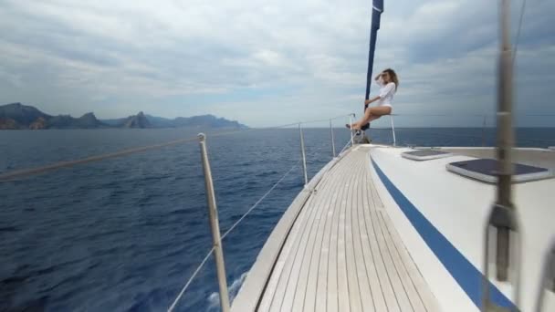 Una hermosa chica mira a la distancia. El viento sopla su cabello, posa y se broncea en un yate. Océano azul . — Vídeos de Stock