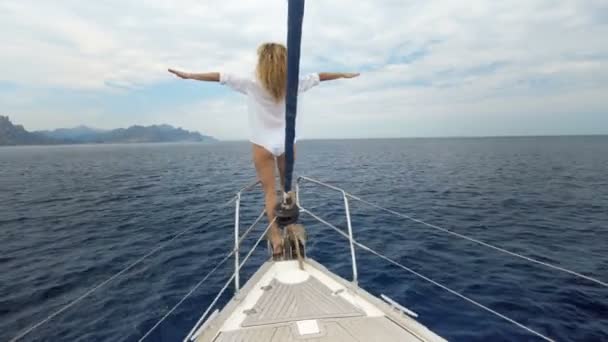 Een mooi meisje ziet er in de verte. De wind waait haar haar, de houdingen en de tans op een jacht. Blauwe oceaan. — Stockvideo