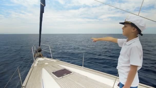 Sommerbild. Ein fröhlicher Junge mit Mütze steht auf der Jacht und zählt die Anzahl der Yachten, die in See stachen. Regatta der Segelyachten. — Stockvideo