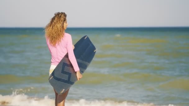 Dziewczyna z kiteboard spaceru wzdłuż plaży tropikalnej plaży o zachodzie słońca. Dziewczynka trzyma w ręku zarządu — Wideo stockowe