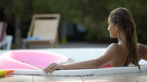 Chica feliz que relaja en flotador rosado inflable del donut. Mujer joven en bikini disfrutando de vacaciones de verano bebiendo cócteles en rosa flotador en la piscina — Vídeo de stock