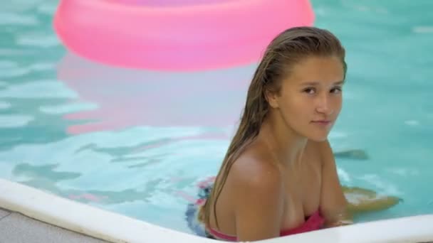 Boldog lány pihentető-úszó felfújható rózsaszín fánk. Fiatal nő a bikini élvezi a nyaralás ivott koktélt a medence rózsaszín floatie — Stock videók