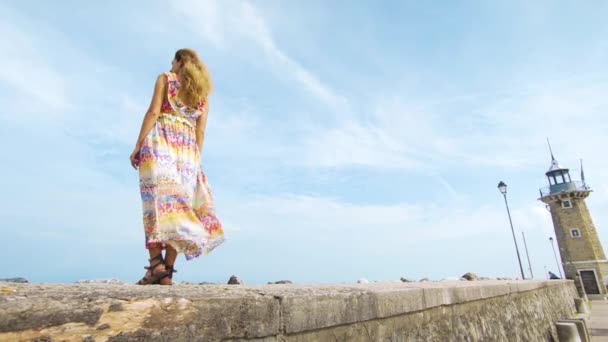 Una ragazza con un vestito è in piedi sull'oceano a guardare il faro — Video Stock