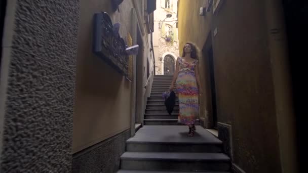 Eine junge Touristin spaziert bei sonnigem Wetter die kleine Straße hinauf. Mädchen verbringt Urlaub in Europa, erkundet die Altstadt. — Stockvideo