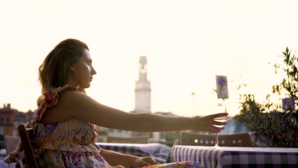 Beleza Jovem bebendo vinho branco e desfrutando de vista para o pôr do sol em um terraço. Menina bonita segurando copo de vinho — Vídeo de Stock