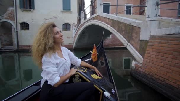 Jonge vrouw in een gondel vaart onder een brug in Venetië — Stockvideo