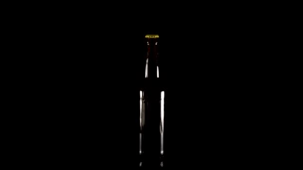 Закрытая бутылка пива вращается на черном фоне — стоковое видео
