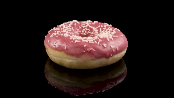 Donut girando com gelo rosa em um fundo preto — Vídeo de Stock