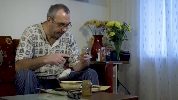 Anciano comiendo comida en casa frente al televisor — Vídeo de stock