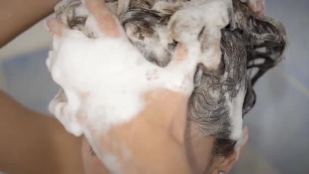 Die junge Frau duscht und wäscht die Haare mit Shampoo. — Stockvideo