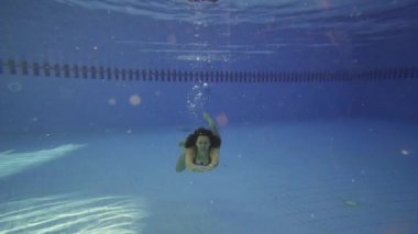 Genç kız yüzme havuzunda su altında yüzüyor. Ağır çekim.