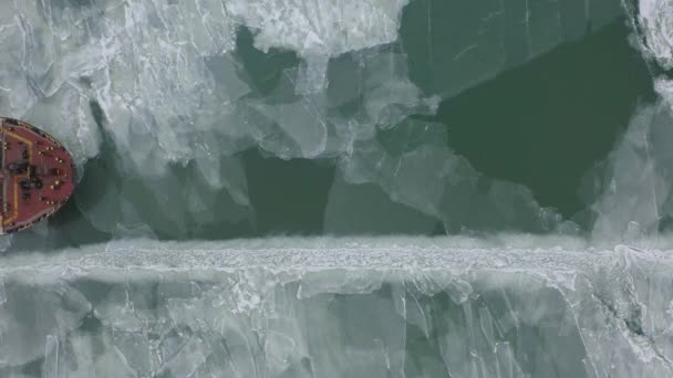 Vrachtschip zeilen op bevroren zee in extreme winter voorwaarden luchtfoto schot. Zeilen in smalle fairway kanaal gemaakt door icebreaker vaartuig. Water transport tijdens de koude winterseizoen in Noord. — Stockvideo