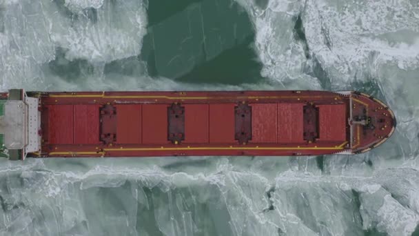 Cargo ship sailing on frozen sea in extreme winter conditions aerial shot. Sailing in narrow fairway channel made by icebreaker vessel. Water transportation during cold winter season in north. — Stock Video