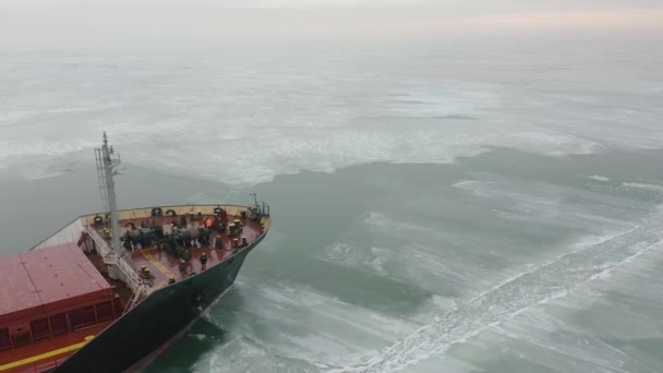 货轮在极端冬季条件下在冰封的海面上航行空中射击。在破冰船制造的狭窄航道航道上航行。北方寒冬季节的水运. — 图库视频影像