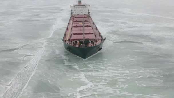 Vrachtschip zeilen op bevroren zee in extreme winter voorwaarden luchtfoto schot. Zeilen in smalle fairway kanaal gemaakt door icebreaker vaartuig. Water transport tijdens de koude winterseizoen in Noord. — Stockvideo