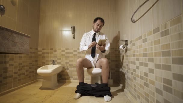 Мужчина сидит на унитазе в роскошном туалете с телефоном и работает. 4k — стоковое видео