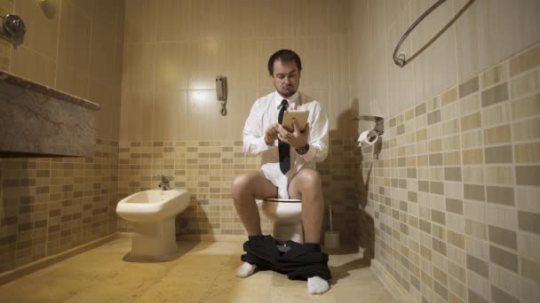 A man sitting on the toilet in a luxurious restroom with a phone and working. 4k — Stock Video