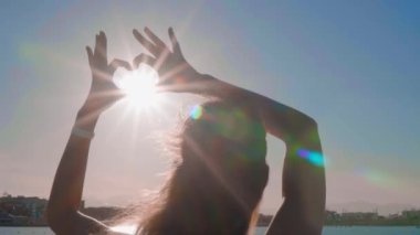 Kız deniz arka plan üzerinde elleriyle kalp olun. Siluet el gün batımı ile kalp şeklinde içinde. Tatil kavramı.