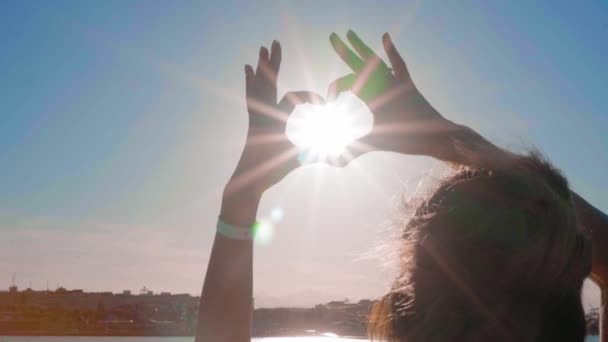 A menina das mãos fez uma forma de coração ao pôr-do-sol, no mar, contra um fundo laranja. Conceito: amor para relaxar no mar, liberdade, amor, estilo de vida, pôr do sol da noite, praia, verão, sol . — Vídeo de Stock