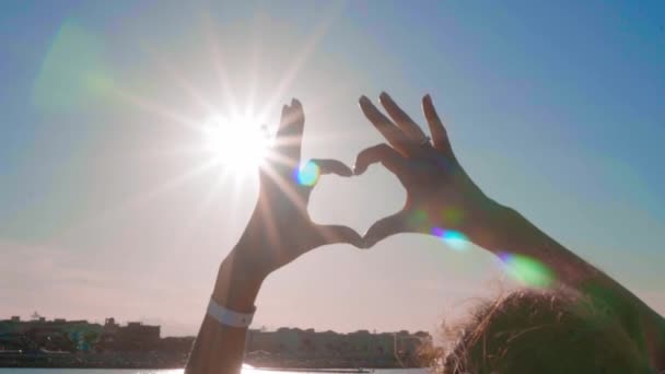 A lányt, hogy szív kezével háttérben tenger felett. Sziluett kéz a szív alakú naplemente benne. Nyaralás koncepció. — Stock videók