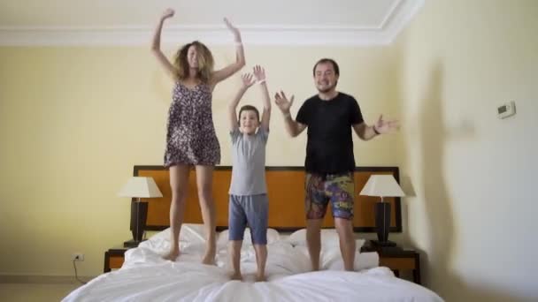 Feliz familia saltando sobre la cama. Concepto familiar feliz. Padre, madre y niño saltan a la cama — Vídeo de stock