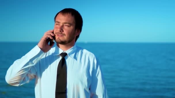 El hombre de negocios en el fondo del hermoso mar hablando por teléfono, resolviendo casos — Vídeo de stock