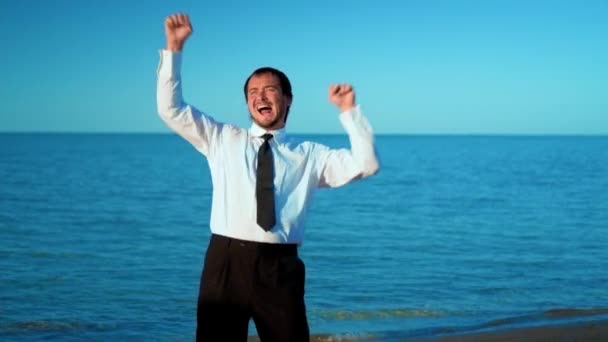 Excited businessman screaming and raising hands to the sky by the sea, slow motion — Stock Video