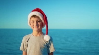 Bir Noel şapkalı bir çocuk denize karşı duran ve gülümseyen
