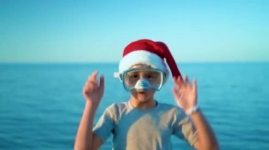 Noel şapkalı çocuk dalış maske ve şnorkel denize karşı duruyor