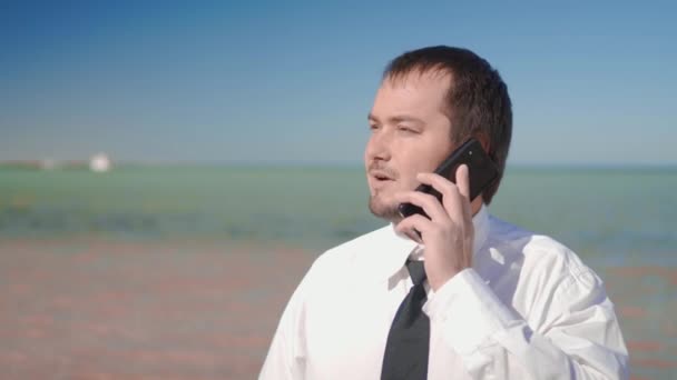 El hombre de negocios en el fondo del hermoso mar hablando por teléfono, resolviendo casos — Vídeo de stock