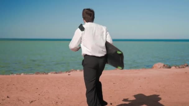 El hombre de negocios de traje corre al mar con una tabla de kitesurf — Vídeo de stock