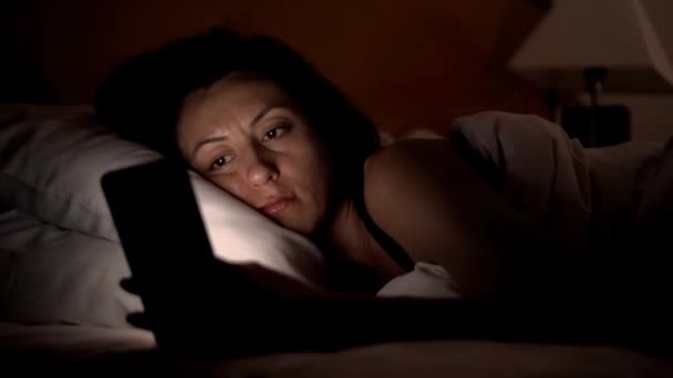 Fiatal nő az ágyban smartphone. Woman főszereplője mobil eszközön, a 4k lefekvés előtt — Stock videók