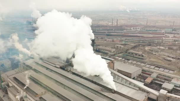 Промышленная зона с большой красно-белой трубой толщиной белого дыма выливается из заводской трубы. Загрязнение окружающей среды: труба с дымом. Вид с воздуха — стоковое видео