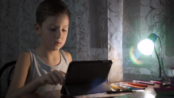 L'enfant utilise la tablette pour étudier, garçon écrivant des devoirs dans l'utilisation d'Internet de nuit 4K — Video