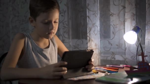 Дитина використовує планшет для навчання, хлопчик пише домашнє завдання в нічному Інтернеті 4K — стокове відео