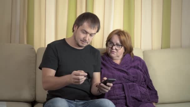Jonge man helpen haar grootmoeder voor met behulp van een digitale Tablet en credit card — Stockvideo